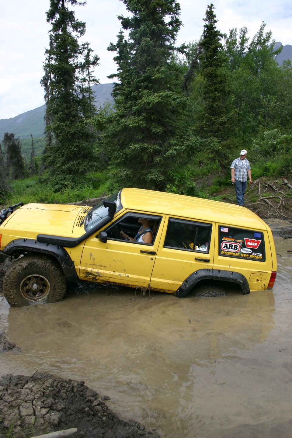 Yellow Jeep Cherokee stuck in mud with ARB stickers on the rear door