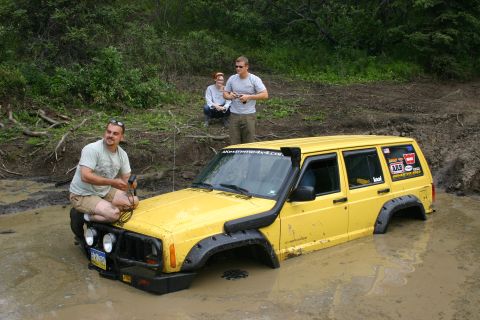 2003 Jeep TJ - A yellow Jeep Cherokee is partially submerged in mud, with people observing.