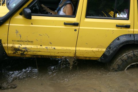 2003 Jeep TJ - A yellow Jeep Cherokee navigates through a muddy, watery terrain, with the 'Cherokee' nameplate visible on its side.