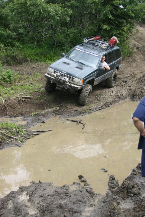 2003 Jeep TJ - A green Jeep Grand Cherokee navigates a muddy off-road course, with a driver visible behind the wheel.