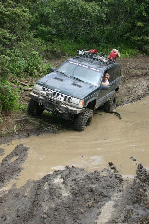 2003 Jeep TJ - A dark green Jeep Grand Cherokee tackles a challenging muddy path, displaying a "KODIAK OFF-ROAD" decal on its windshield.