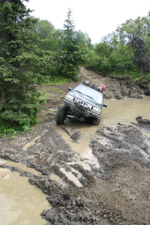 2003 Jeep TJ - This Jeep Grand Cherokee is navigating a challenging muddy trail, with one wheel significantly turned.