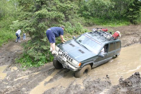 2003 Jeep TJ - Jeep Grand Cherokee navigating a challenging muddy trail, with onlookers observing the off-road adventure.