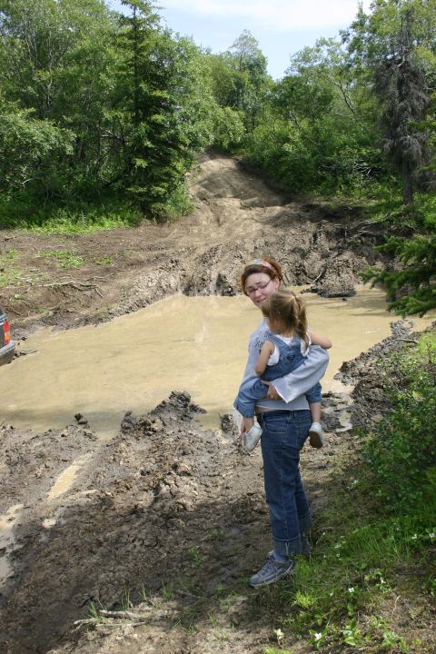2003 Jeep TJ - A woman holds a child while standing next to a large mud puddle on a challenging off-road trail.