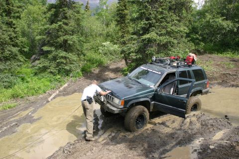 2003 Jeep TJ - A man attempts to free a green Jeep Grand Cherokee from a muddy off-road track.