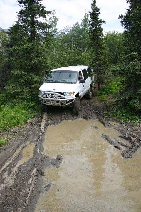 2003 Jeep TJ - A white van drives through a large mud puddle on a wooded trail.