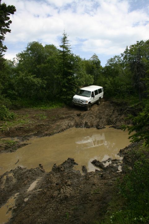 2003 Jeep TJ - A white van navigates a challenging muddy path through a wooded area.