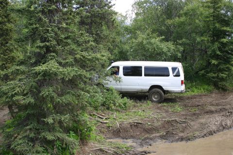 2003 Jeep TJ - A white van navigates a muddy, off-road path through a wooded area.