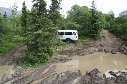 2003 Jeep TJ - Van stuck on a challenging muddy off-road path surrounded by dense forest.