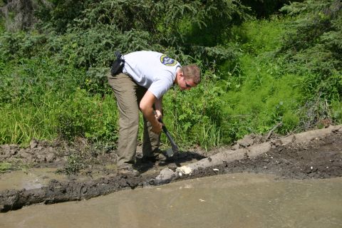 2003 Jeep TJ - A person is digging in a muddy area with vegetation in the background.
