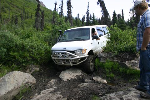 2003 Jeep TJ - A white van navigates a challenging off-road trail with rocky terrain and dense vegetation.