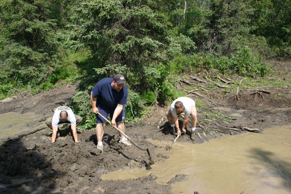 Three men working in a muddy area with trees in the background