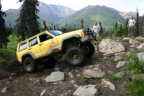 2003 Jeep TJ - A yellow Jeep Cherokee XJ navigates a challenging off-road trail in a mountainous, wooded area.