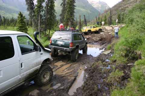 2003 Jeep TJ - Multiple off-road vehicles traverse a challenging muddy path in a mountainous, wooded area.