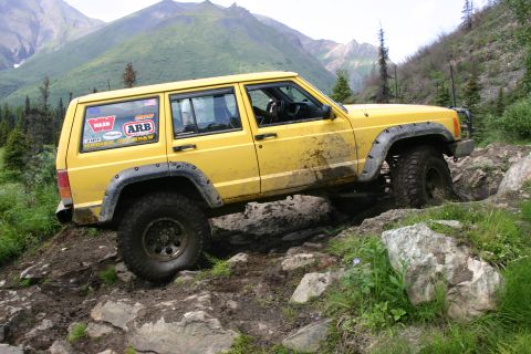 2003 Jeep TJ - A yellow Jeep Cherokee XJ navigates a challenging rocky terrain, demonstrating its off-road capabilities.