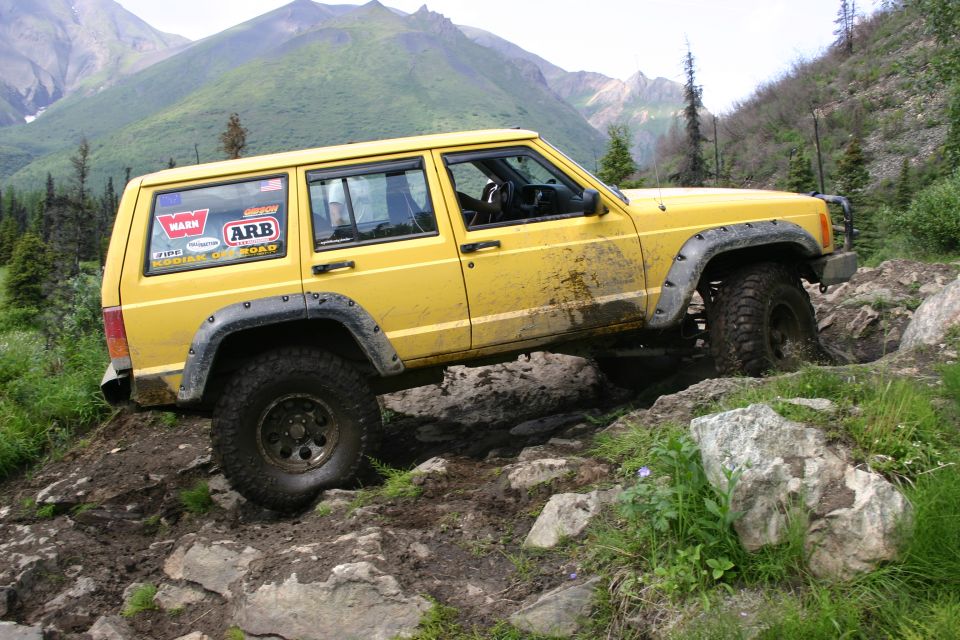 Yellow Jeep Cherokee XJ off-roading on a rocky trail, mud splattered on its side