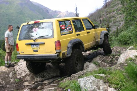 2003 Jeep TJ - Yellow Jeep Cherokee XJ tackling a challenging rocky trail with a person standing nearby.