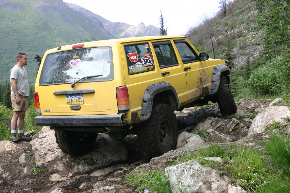 Yellow Jeep Cherokee XJ with off-road tires navigating rocky terrain. License plate ELK 785