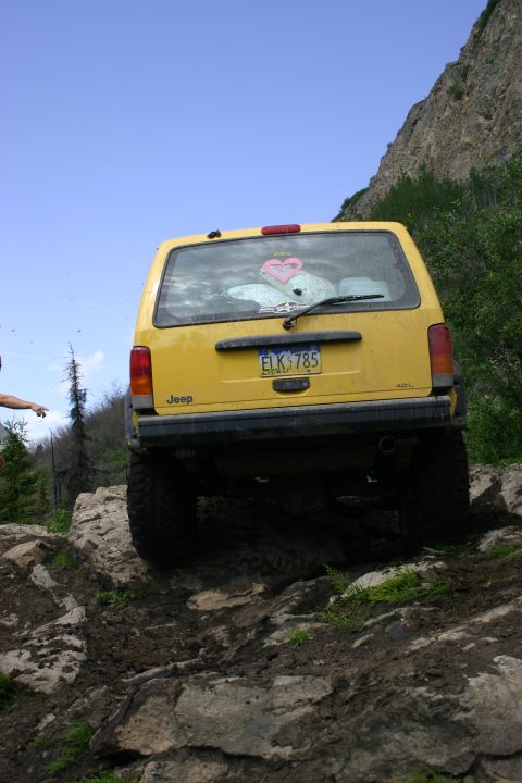 2003 Jeep TJ - A yellow Jeep Cherokee XJ navigates a challenging off-road path with steep, rocky terrain.