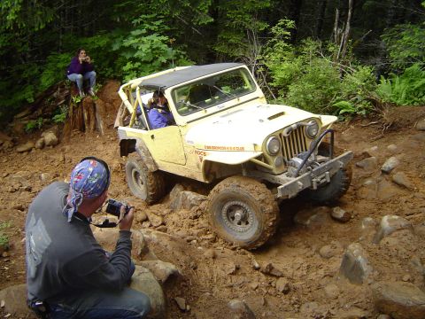 1989 Ford Bronco - A yellow off-road vehicle navigates a muddy trail while a photographer captures the moment.