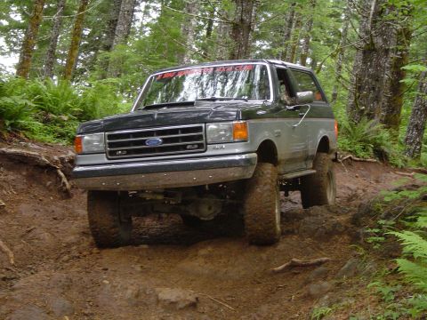 1989 Ford Bronco - Ford Bronco navigates a challenging muddy path through a wooded area.