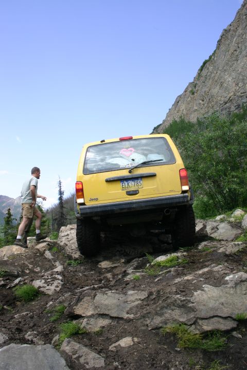 2003 Jeep TJ - A yellow Jeep Cherokee navigates a challenging rocky terrain on an off-road trail.