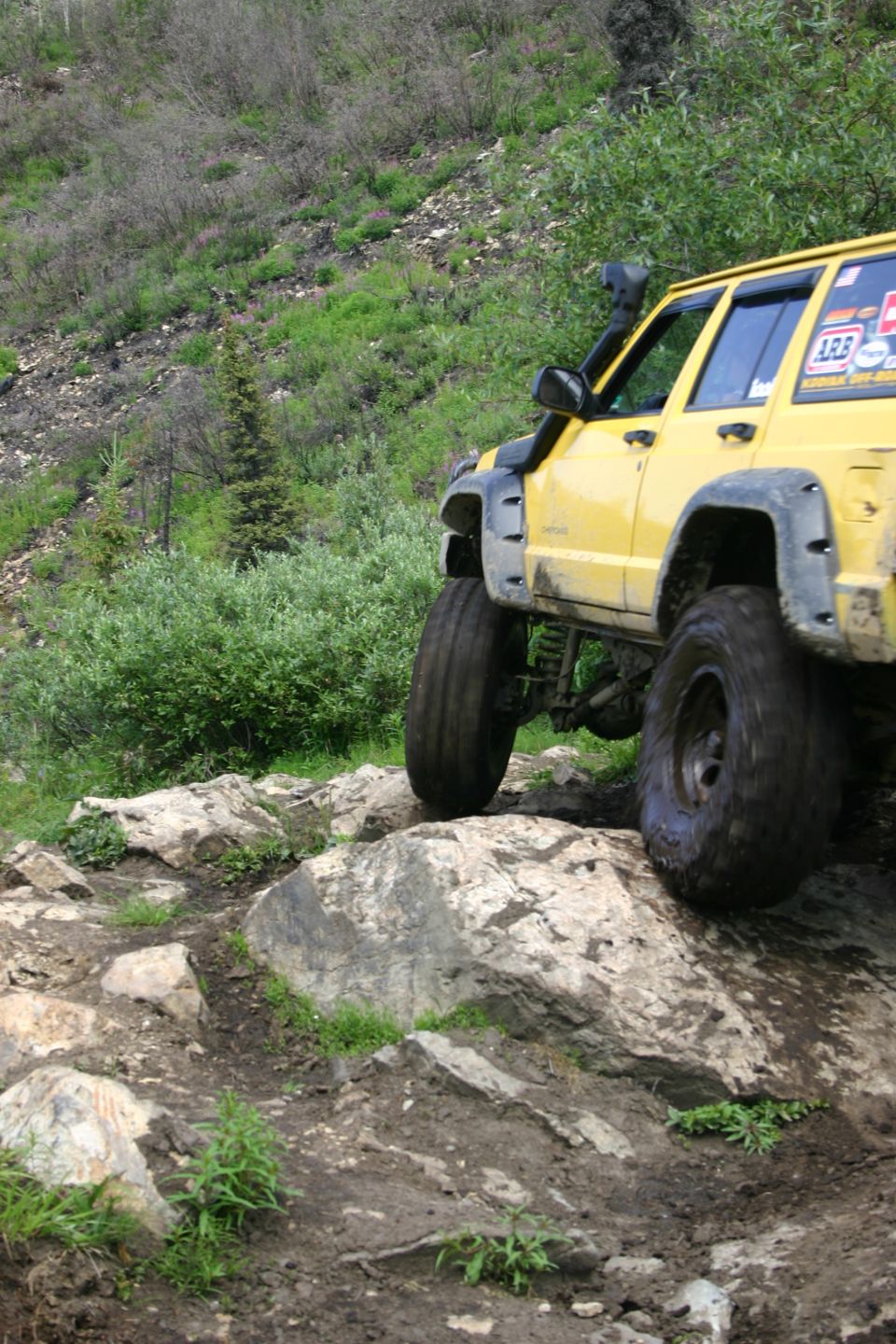 Yellow SUV with snorkel and off-road tires climbing over rocks on a trail