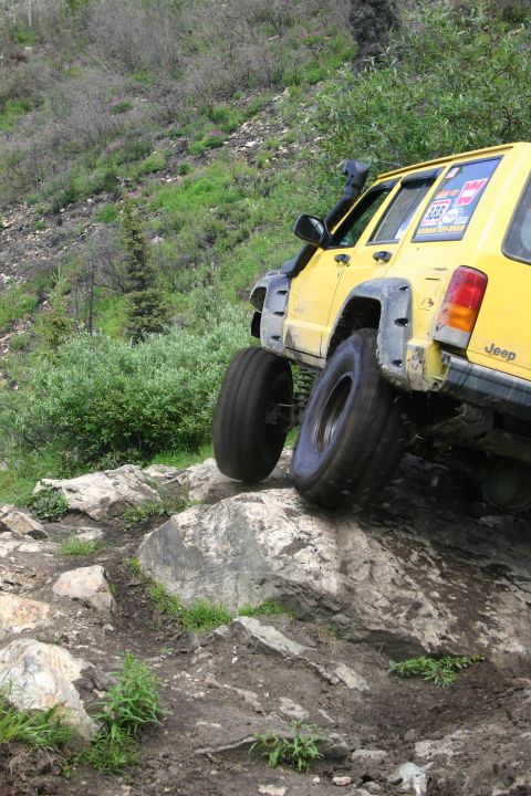 2003 Jeep TJ - A yellow Jeep Cherokee XJ navigates a challenging rocky trail, its tires angled on large boulders.