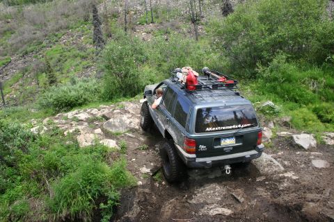 2003 Jeep TJ - This Jeep Grand Cherokee navigates a challenging rocky trail, equipped with a roof rack and extra fuel can.