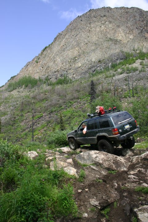 2003 Jeep TJ - A dark green Jeep Grand Cherokee navigates a challenging rocky path on a mountainside.
