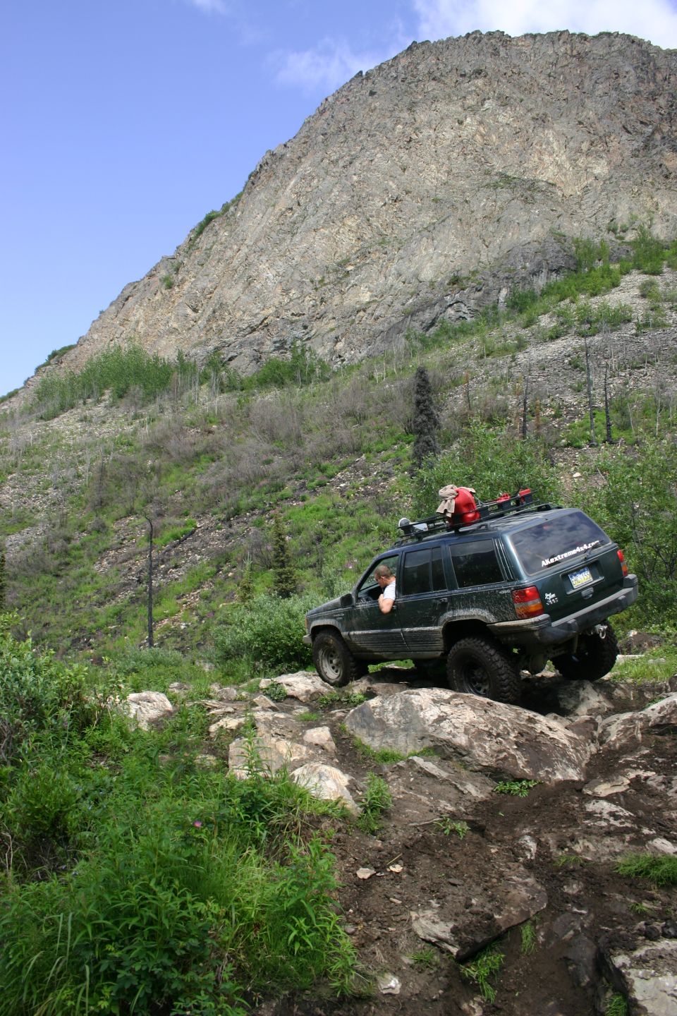 Dark green Jeep Grand Cherokee climbing a rocky trail, roof rack loaded