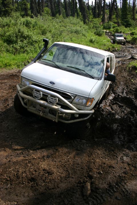 2003 Jeep TJ - This van is navigating a challenging muddy off-road trail with a second vehicle in the background.