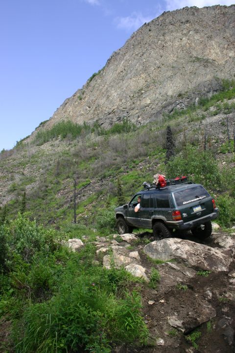 2003 Jeep TJ - An SUV tackles a challenging rocky terrain on an incline, with a large mountain face dominating the scenery.