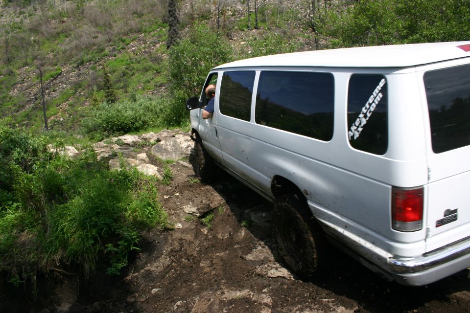 White van with 'akextreme4x4.com' sticker navigating a rocky, muddy trail