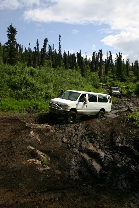 2003 Jeep TJ - Two off-road vehicles tackle a difficult muddy path through a wooded area.