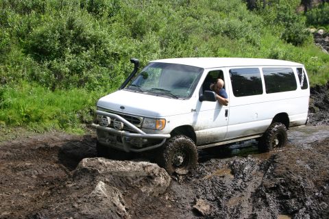 2003 Jeep TJ - A white van with a snorkel and brush guard drives through a muddy, off-road course.