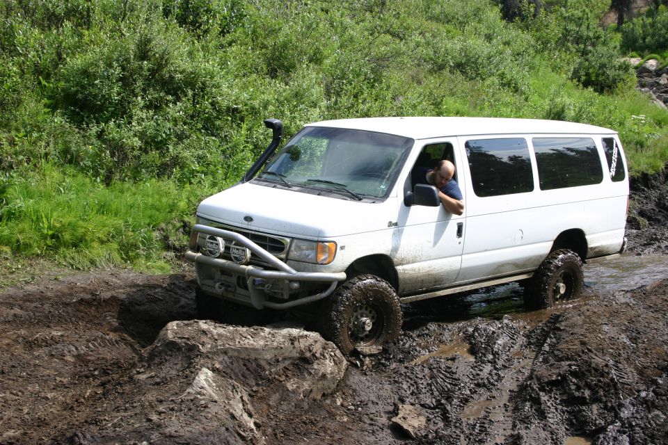 White van with off-road tires and a brush guard navigating a muddy trail
