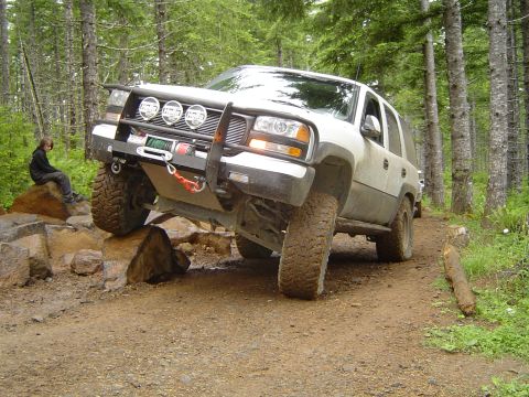 1989 Ford Bronco - White SUV with off-road modifications navigating a rocky trail in a forest.