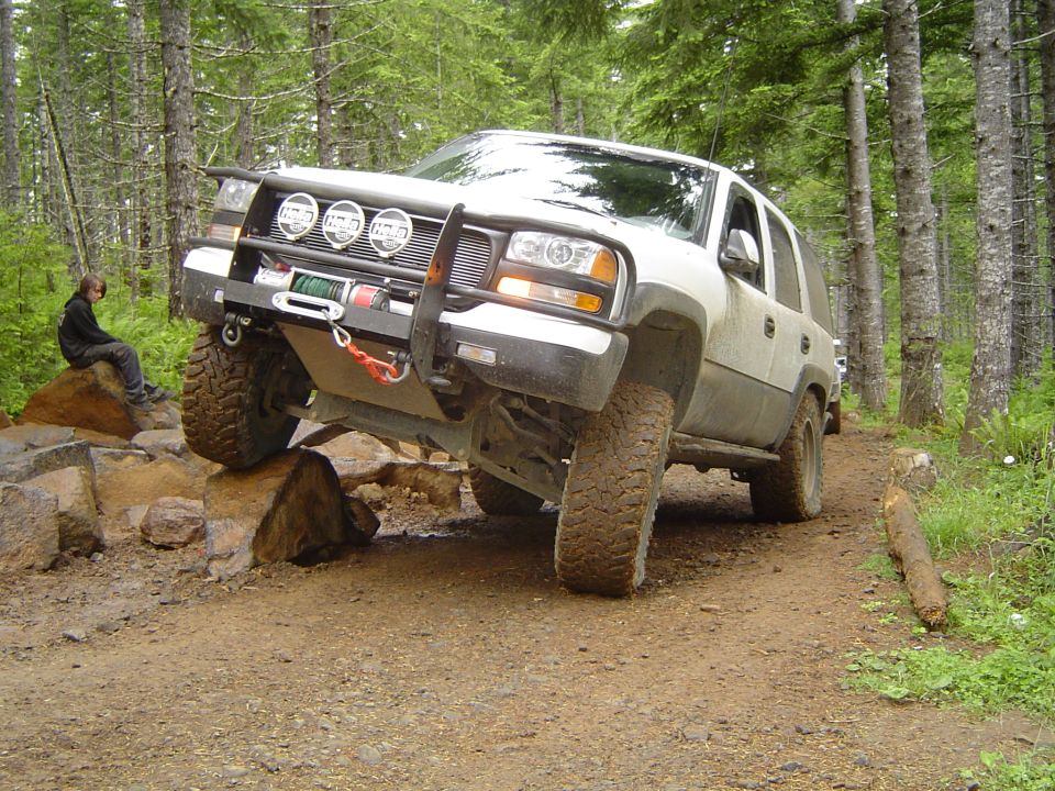 White Chevy Tahoe with winch bumper climbing rock ledge on forest trail