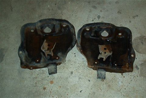 1986 Ford Bronco - These two heavily rusted metal brackets are shown lying on a concrete surface.