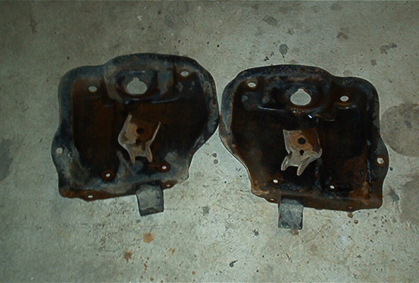 Two rusty metal brackets with mounting points, likely from a vehicle's undercarriage