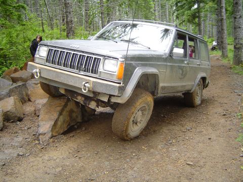 1989 Ford Bronco - A Jeep Cherokee XJ navigates a challenging rocky path in a wooded area.