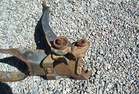 1986 Ford Bronco - Close-up of a heavily rusted vehicle suspension part lying on gravel.