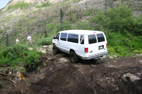 2003 Jeep TJ - A white van navigates a challenging off-road trail with steep, vegetated hillsides.