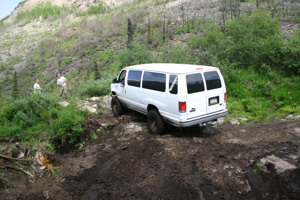 White van with off-road tires driving on a muddy, rocky incline