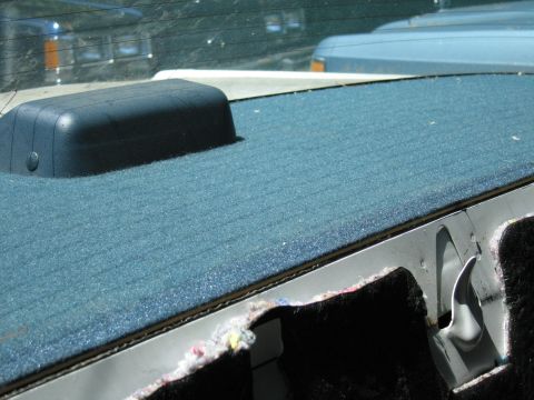 1991 Ford LTD Crown Victoria - The interior rear deck of a car, showing a blue carpeted surface and a black speaker cover, with other vehicles visible through the rear wi…
