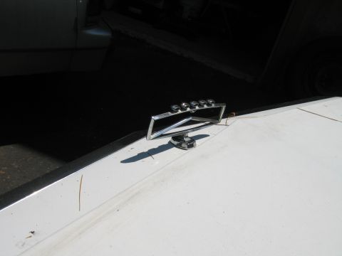 1991 Ford LTD Crown Victoria - A chrome hood ornament with five studs is visible on the hood of a white vehicle, with another vehicle partially visible in the background.