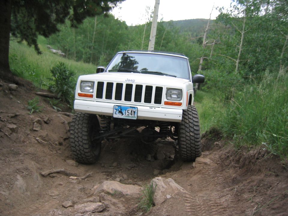 White 1997 Jeep Cherokee driving on a rocky, wooded trail