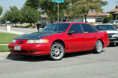 1993 Ford Taurus - This 1993 Ford Taurus sedan features a contrasting black hood and aftermarket wheels, parked curbside.