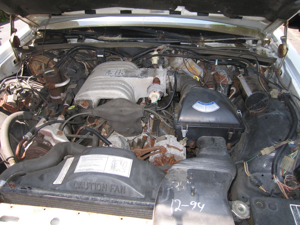 Engine bay with visible engine components and wiring. 'CAUTION FAN' text on shroud. '12-94' handwritten on black plastic